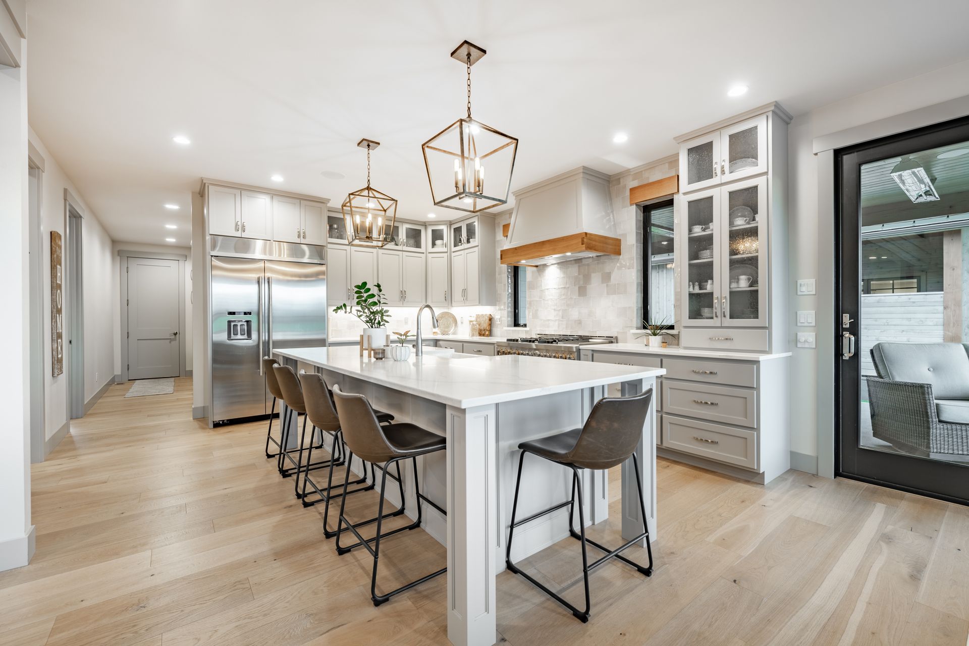Modern kitchen with large island and stainless steel appliances; light wood flooring and gray cabinets.