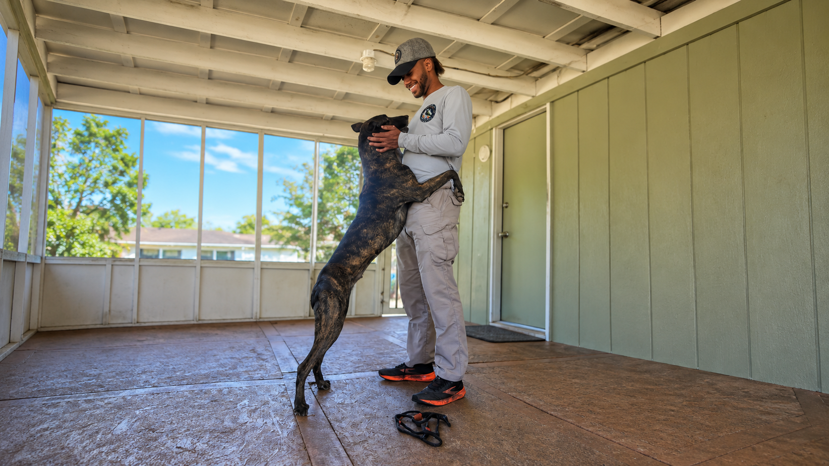 Person in a white uniform stands with a large black dog in a covered outdoor training area.