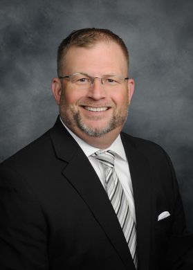 Portrait of a smiling man in a black suit and striped tie against a gray studio backdrop