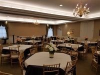 Elegant banquet hall with round tables, gold chairs, and chandeliers under soft lighting