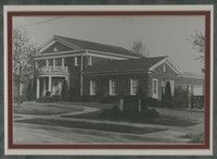 Black-and-white photo of a brick funeral home with a front porch, trees, and a lawn