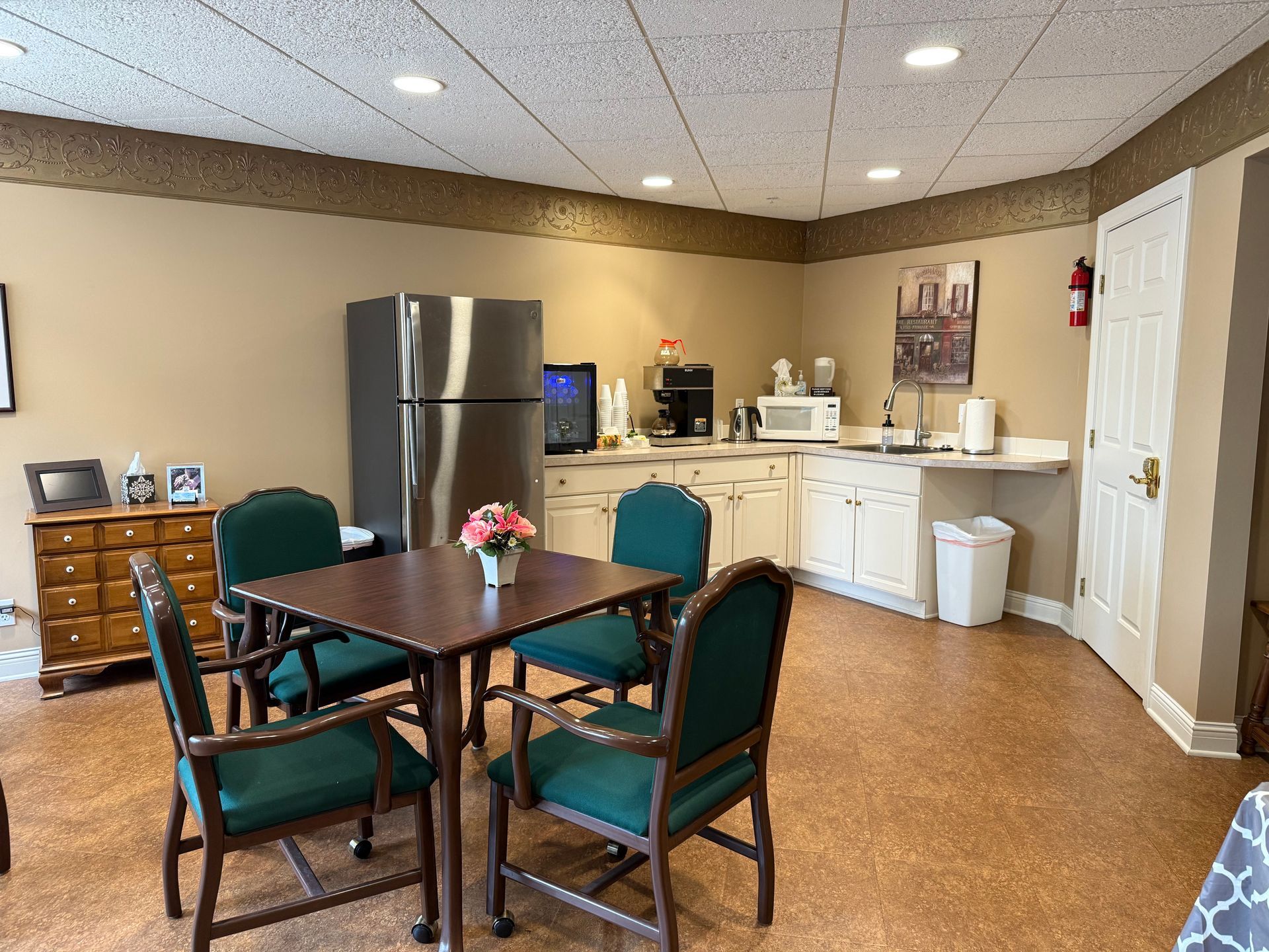 Dining area with table and chairs, stainless refrigerator, and kitchenette with coffee station.