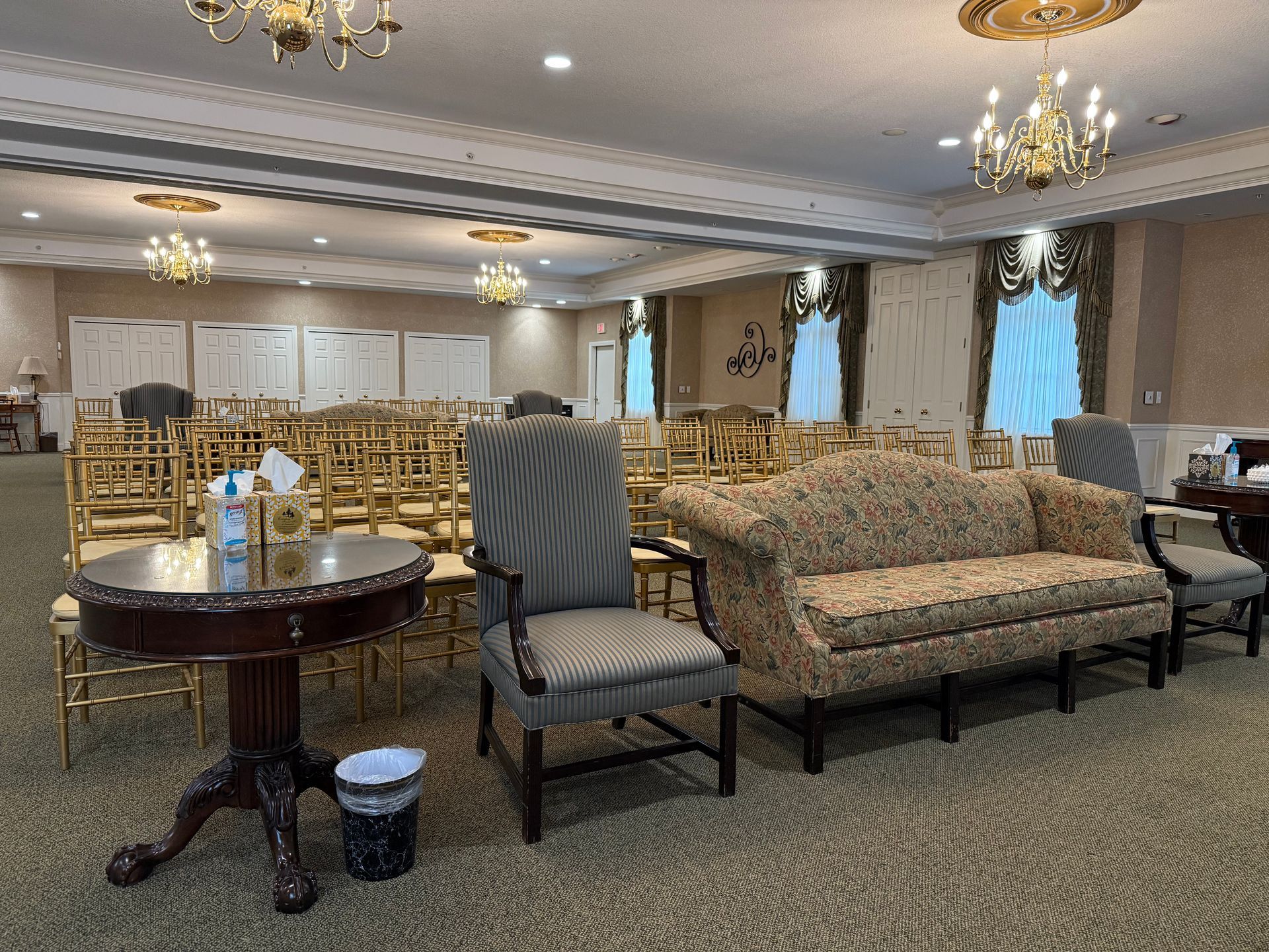 Elegant lounge with patterned sofas, upholstered chairs, tables, and chandeliers in a spacious hall