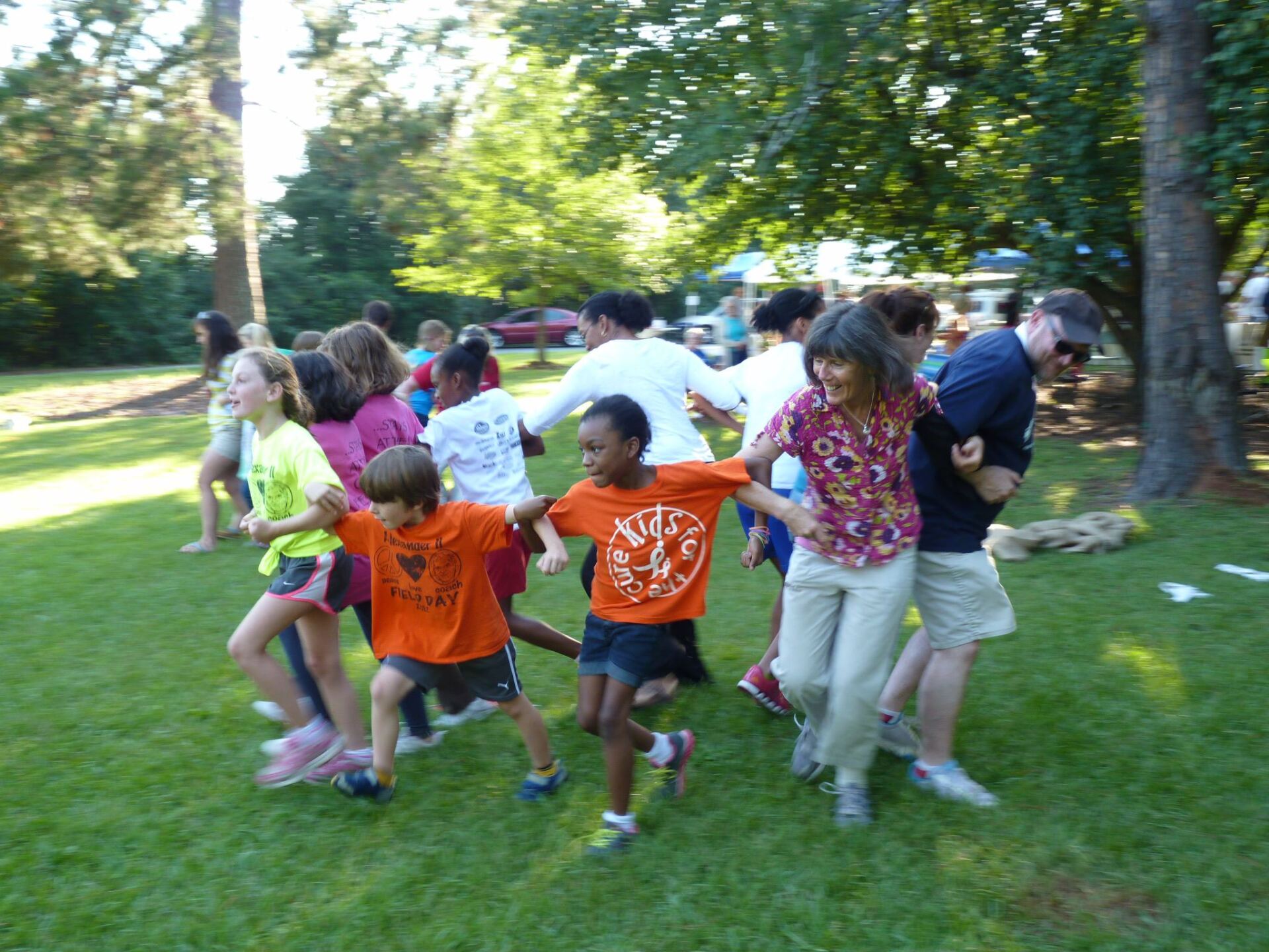 A group of children and adults in a line playing a game on a grassy field outdoors.