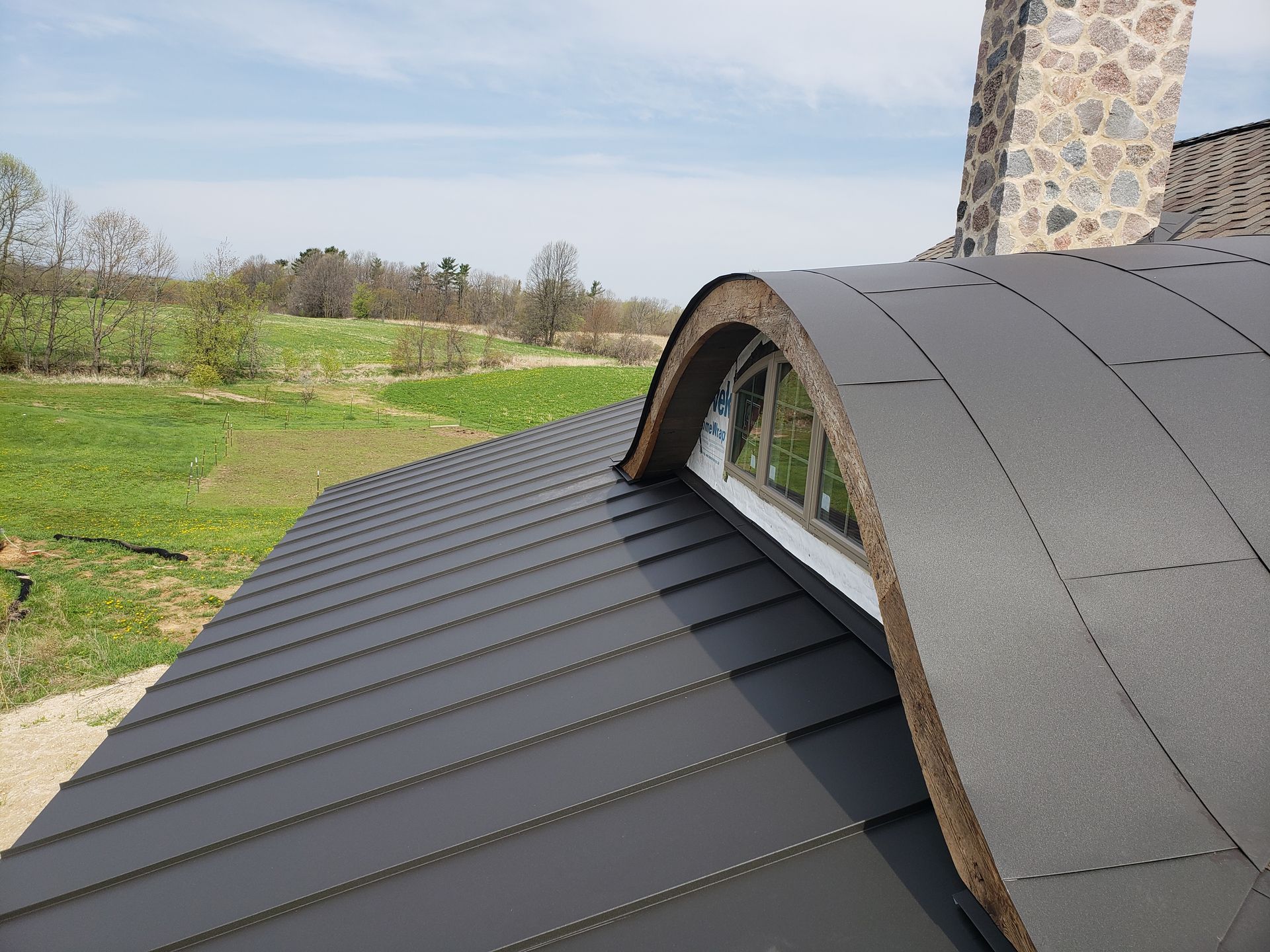 A black roof with a curved window and a stone chimney