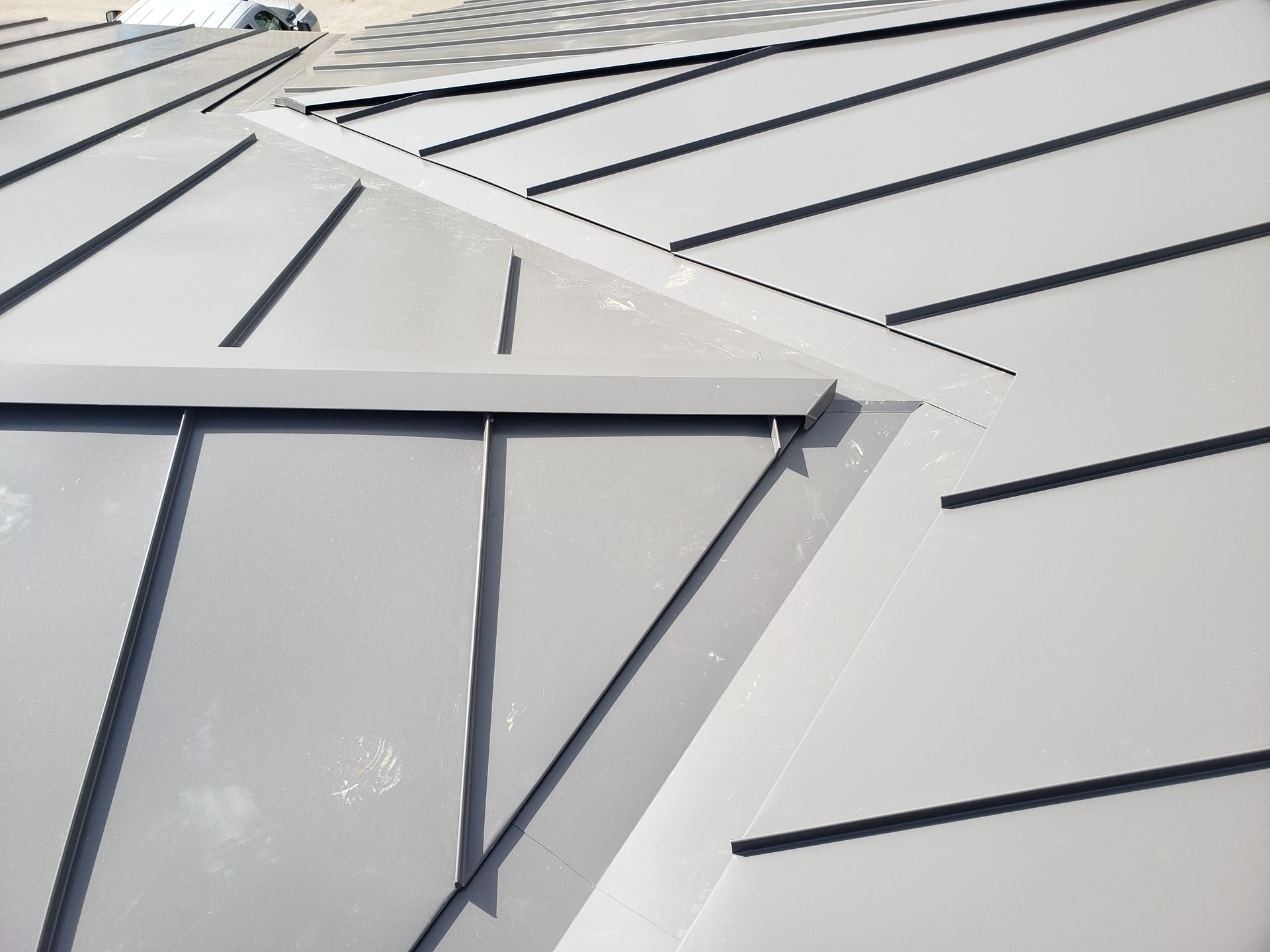 Close-up of a gray metal roof with intersecting panels and seams, angled sunlight.