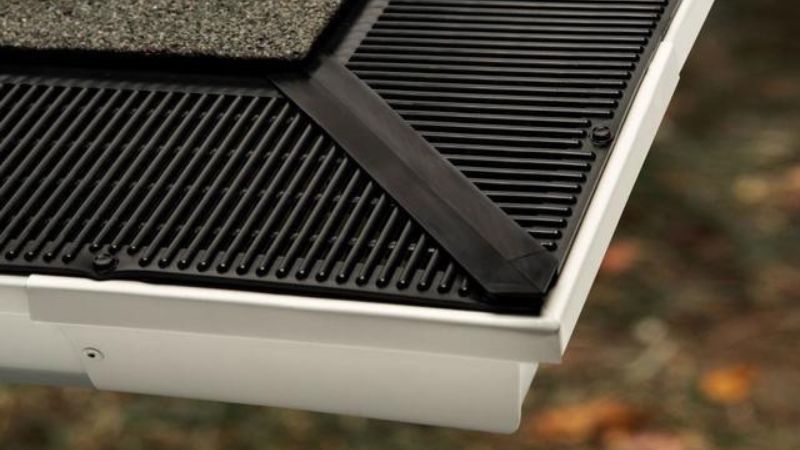 A close up of a gutter on a roof with a black grate.