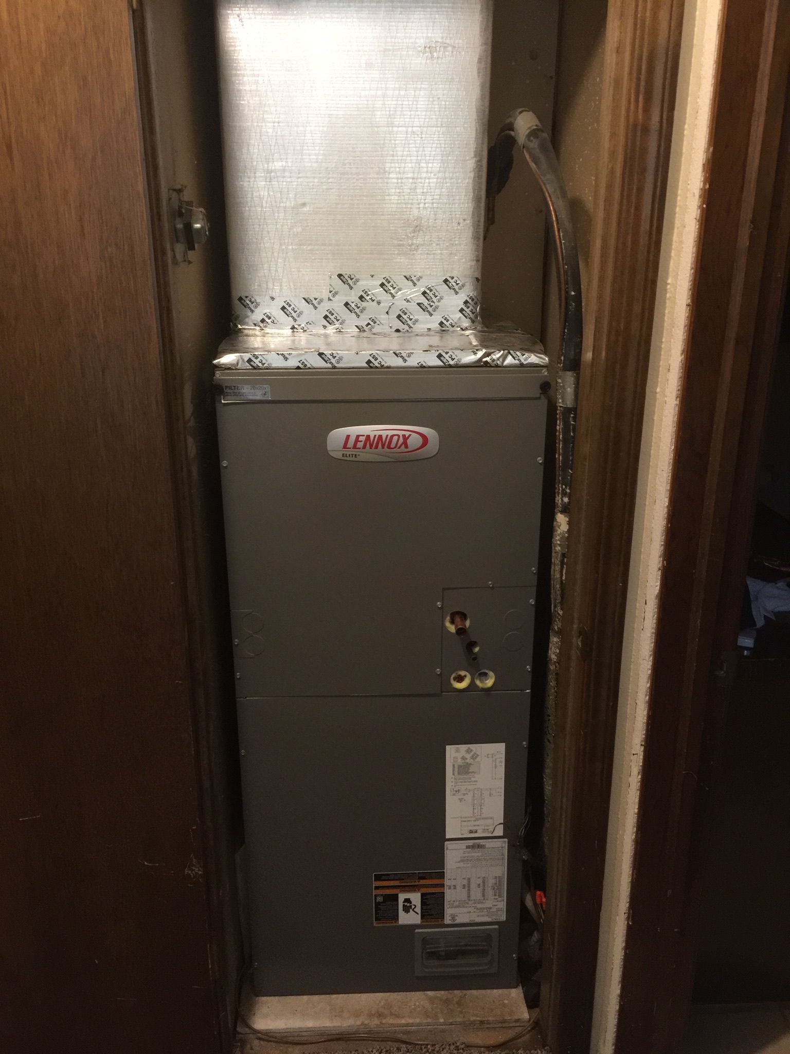 A lennox air conditioner is sitting in a closet next to a door.