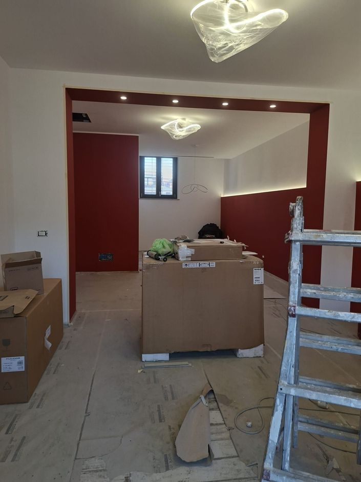Stanza ristrutturata con scatole di cartone, scala e pavimento non rifinito sotto le luci a soffitto.