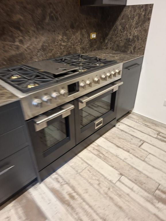 Cucina moderna con piano cottura a gas in acciaio inox e forno, con paraschizzi effetto marmo scuro e mobili scuri.