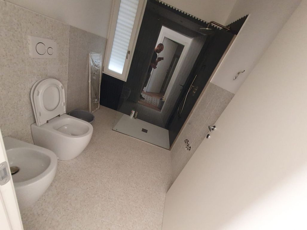 Bagno moderno con WC bianco, lavabo e grande specchio con cornice nera accanto alla doccia.