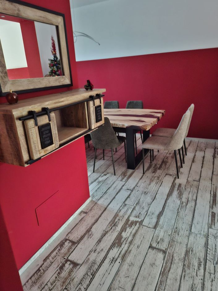 Sala da pranzo con pareti rosse, tavolo in legno, sedie bianche e mensola a muro sotto uno specchio.