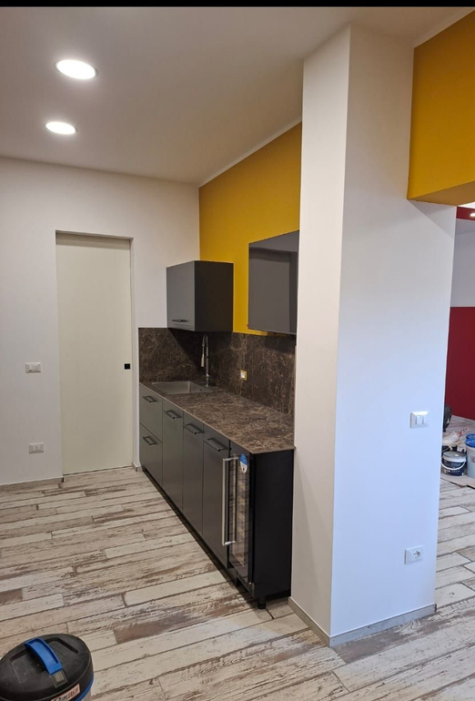 Cucina moderna con dettagli gialli, mobili grigi, paraschizzi a motivi geometrici e una piccola lavatrice.