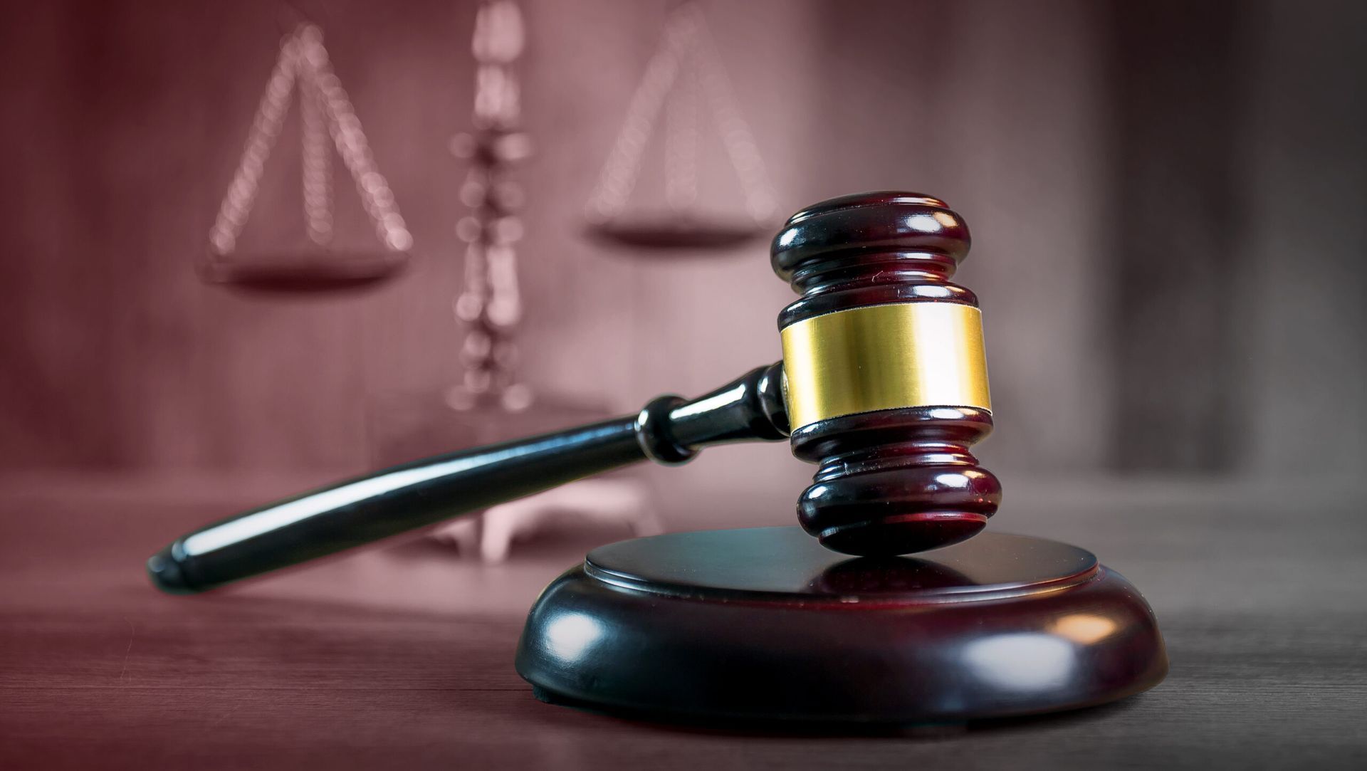 A wooden gavel rests on a round base with scales of justice blurred in the background.