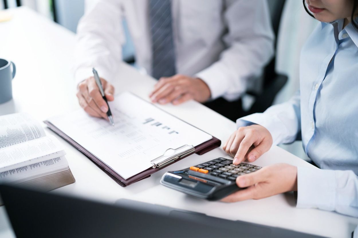 Two office professionals reviewing documents and using a calculator at a desk.
