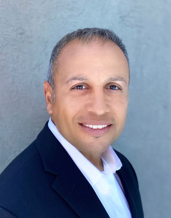Man in a dark blazer smiling, with a white collar shirt.