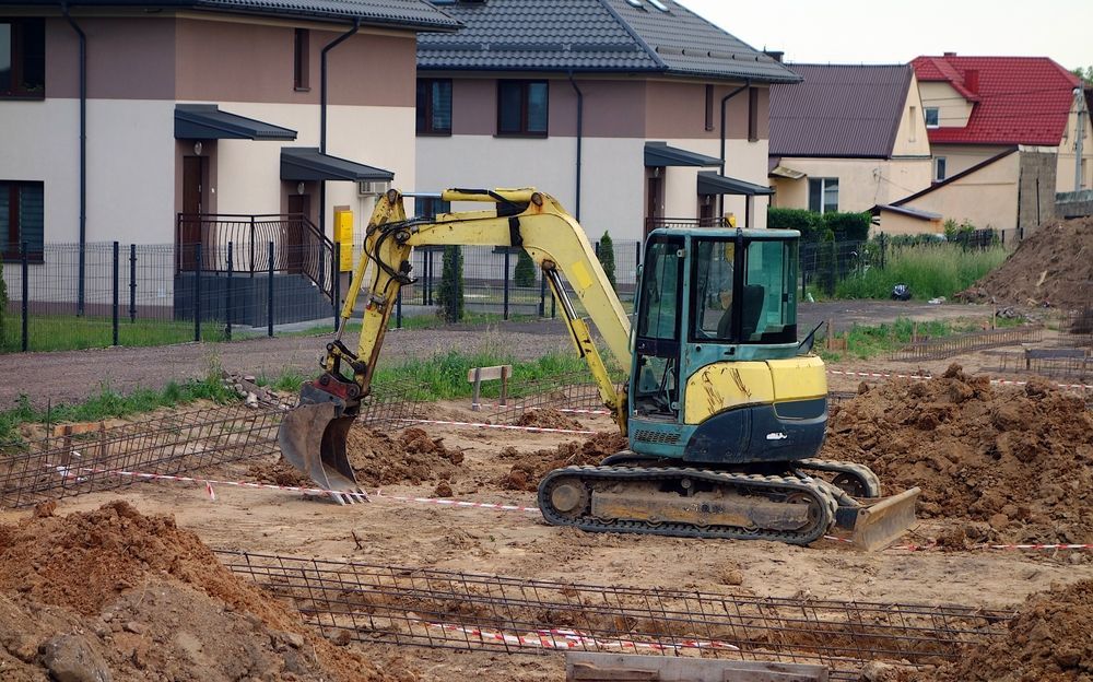 Yellow Excavator at a Construction Site, With Houses — Kellie O'Malley Conveyancing In Lake Macquarie, NSW