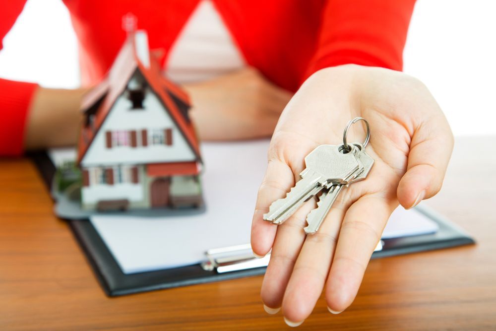 Hand Holding Keys, Miniature House, and Documents on a Desk 	— Kellie O'Malley Conveyancing In Cessnock, NSW