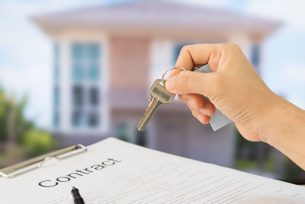 Hand Holding Keys Above a Contract, House in Background — Kellie O'Malley Conveyancing In Singleton, NSW