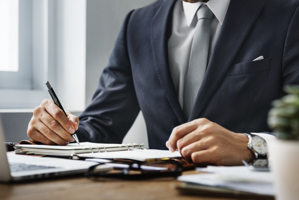 Man in Suit Writing in a Notebook at a Desk — Kellie O'Malley Conveyancing In Lake Munmorah, NSW