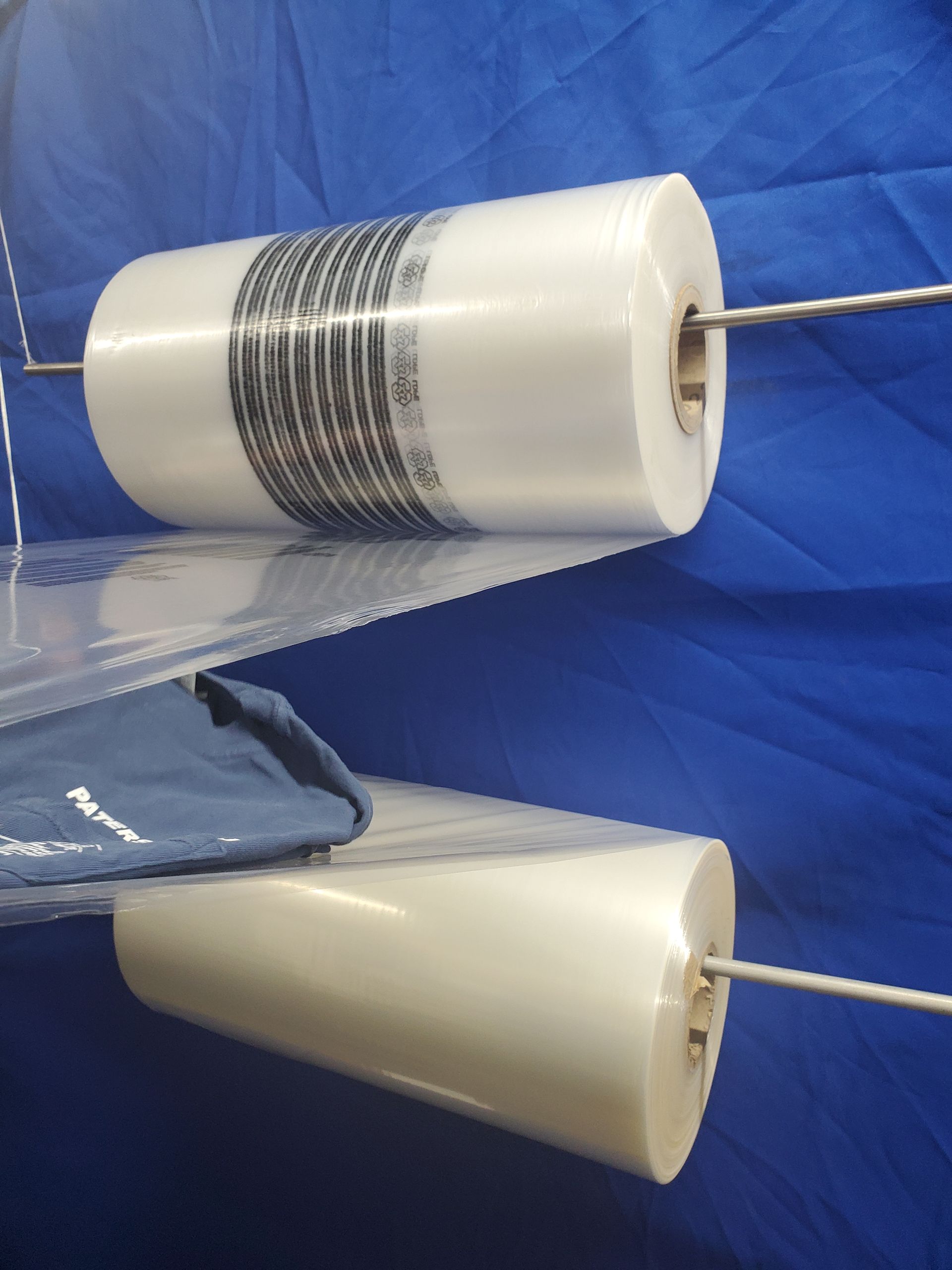 Two rolls of clear plastic bags, one with a barcode label, mounted on rods, against a blue backdrop.
