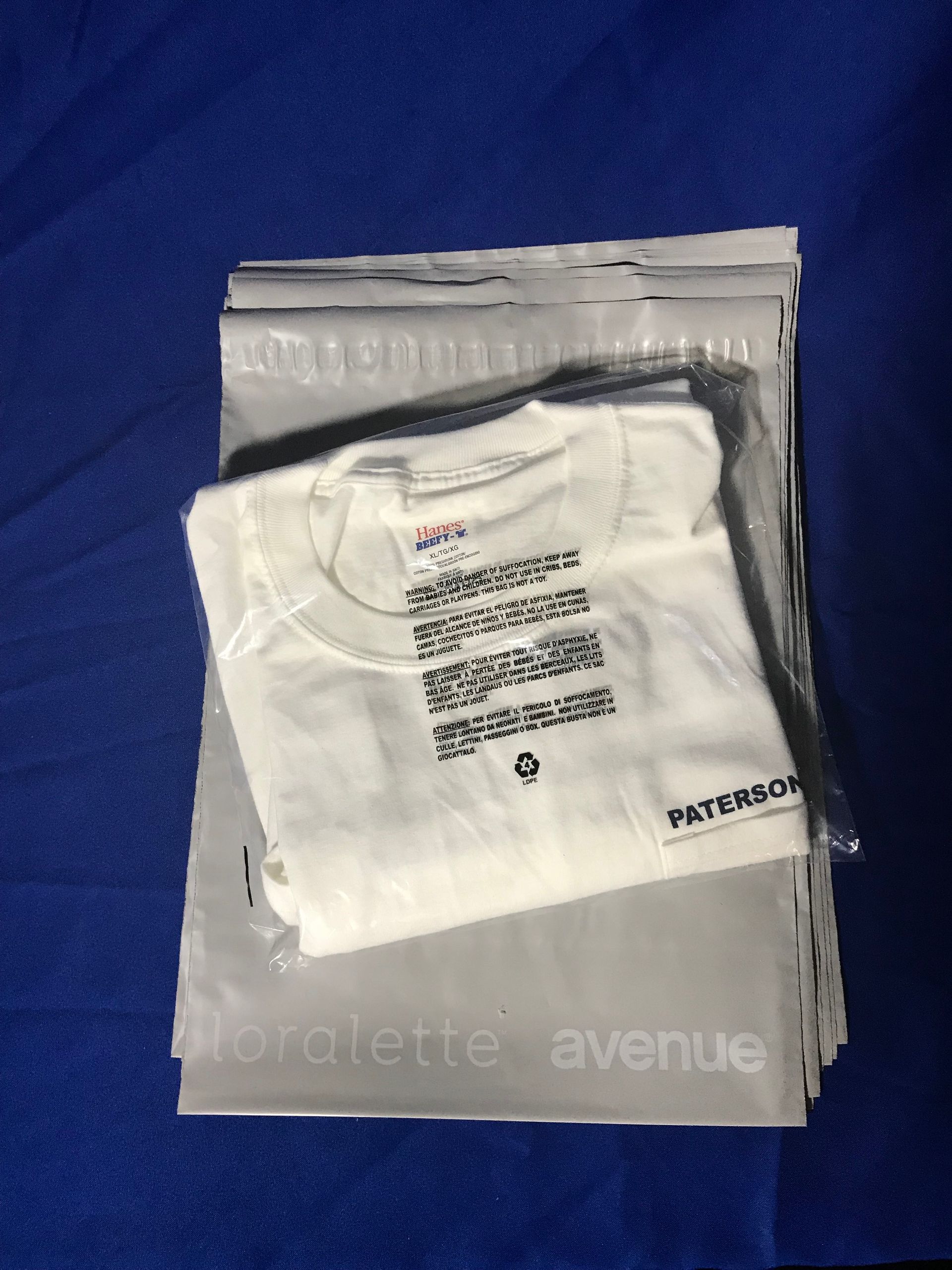 White t-shirt with black text on top of gray shipping mailers on a blue surface.