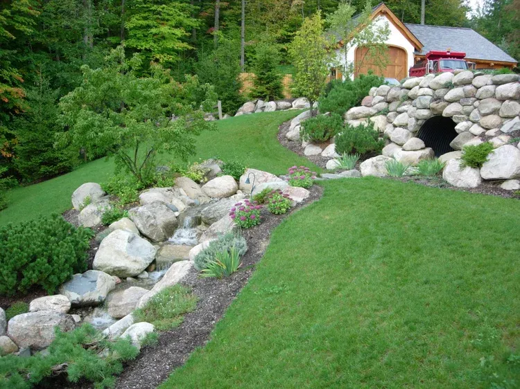 Curved driveway beside lush garden beds with pink and white flowers and a tree