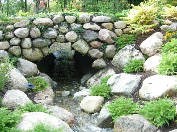 Stone arch bridge over a small stream in a lush green garden
