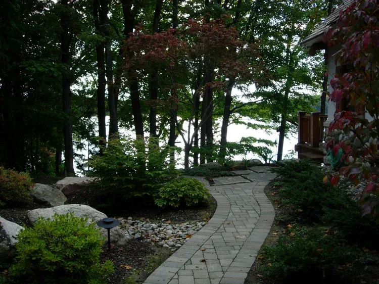 Stone garden path curving through trees toward a bright lakeside view