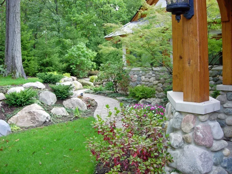 Garden path beside stone landscaping and wooden porch posts amid lush green trees