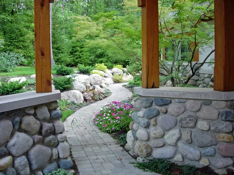 Stone garden path under a wooden pavilion, leading through lush greenery and flowers.