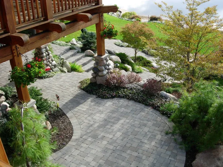 Curved stone patio with landscaped garden, wooden deck, rocks, shrubs, and flowering plants