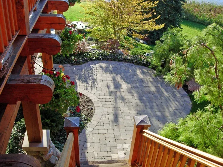 Wooden deck stairs overlooking a curved stone patio and lush green garden below