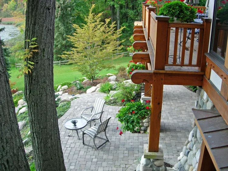Wooden deck overlooking a lush garden with patio chairs, table, and hanging flower baskets