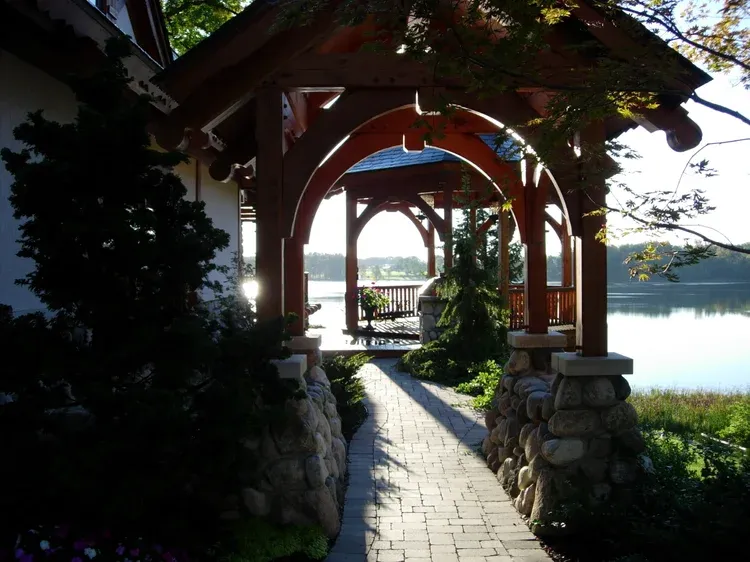 Sunlit stone path leading through a wooden archway toward a bright waterfront view