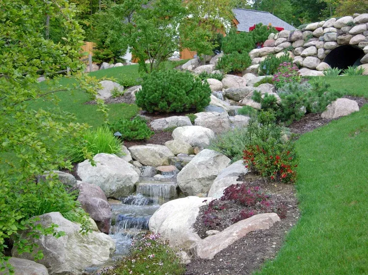 Rock garden with a small cascading stream, green shrubs, and a stone bridge