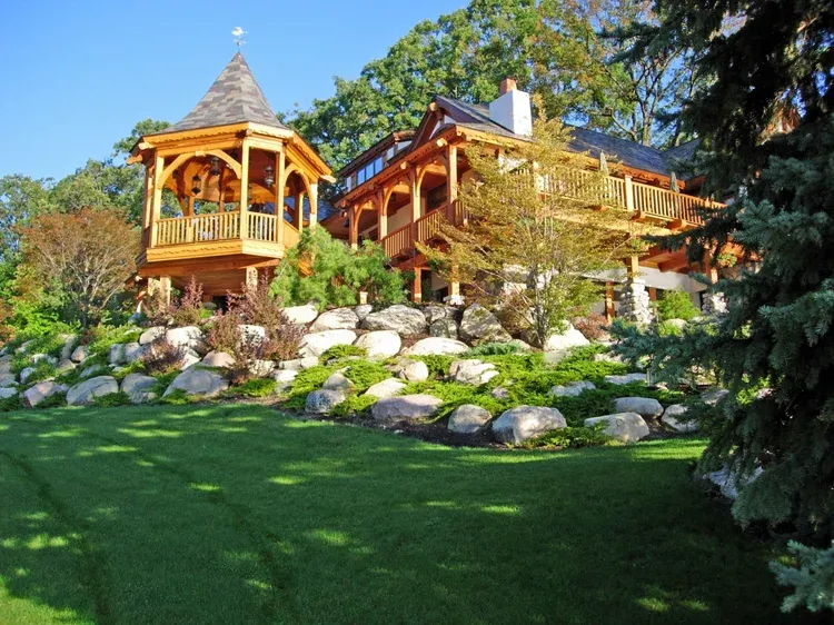 Two wooden gazebos on a landscaped hillside with rocks, trees, and green lawn