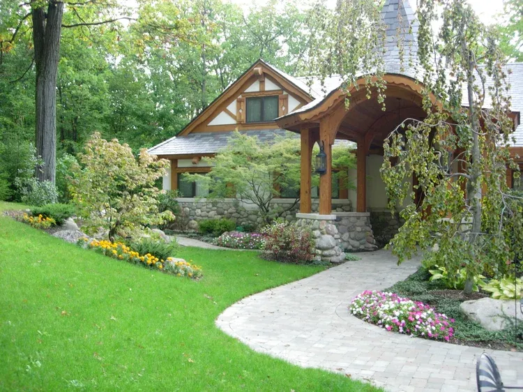 Wooden cottage with arched porch in a lush garden, bordered by green lawn and flowers
