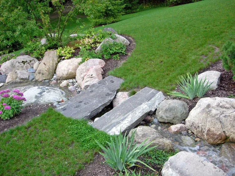 Rock garden with boulders, stepping stones, and green lawn beside a landscaped slope