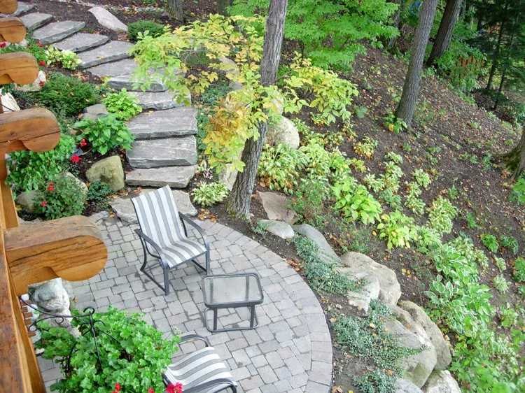 Stone patio with striped chairs beside a landscaped garden and steps lined with flowers and greenery