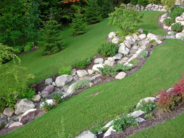 Rock-lined dry stream bed winding through a lush green landscaped hillside garden