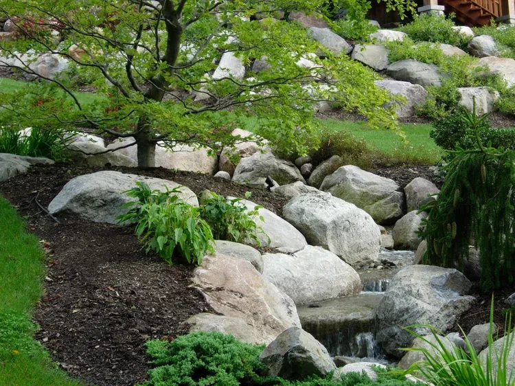 Rock garden with large white stones, green shrubs, and a small stream flowing through it