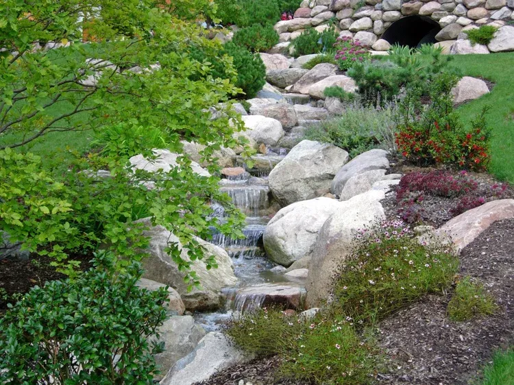 Garden stream with rocks, green trees, and a small stone arch at the top