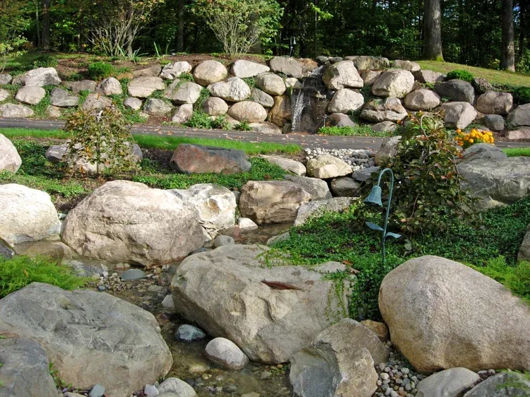 Rock garden with large stones, low terraced rock wall, and green plants in a wooded setting
