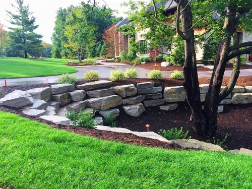 Stone retaining wall beside a landscaped lawn, path, and trees in a garden courtyard