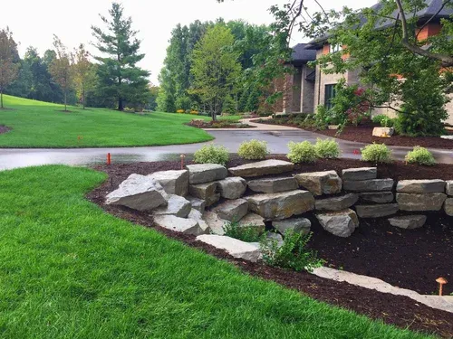 Curved stone retaining wall beside a lush green lawn and landscaped garden path with trees and shrubs
