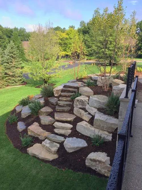 Stone retaining wall with large boulders on a landscaped hillside beside a lawn and trees