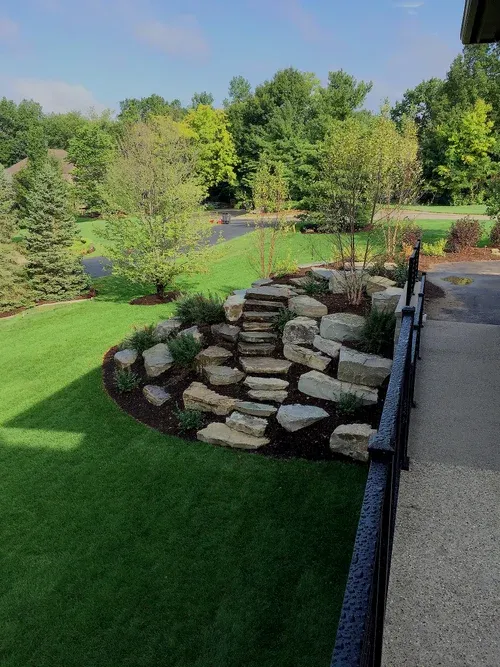 Backyard patio with a stone retaining wall, green lawn, and trees beside a pond