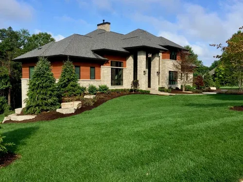 Stone house with a dark roof, green lawn, and landscaped yard on a sunny day