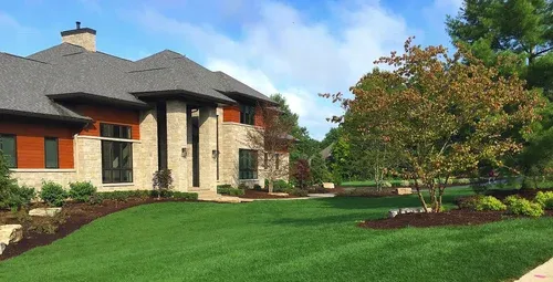 Stone house with red shutters and a manicured green lawn under a blue sky